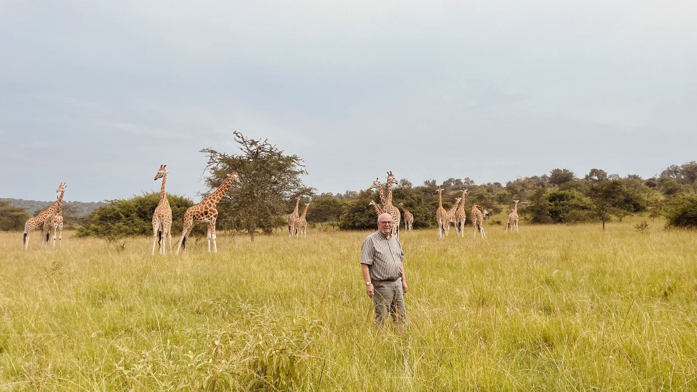 Guest standing in golden grassland with a herd of giraffes in the distance