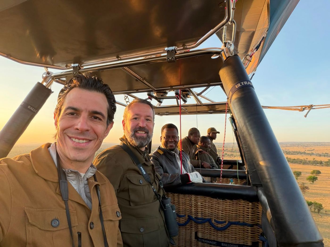 Guests and pilot in a hot air balloon at sunrise over the Serengeti plains
