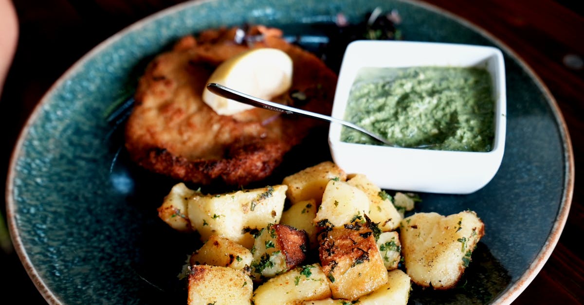 Plate of schnitzel, roasted potatoes, and green sauce, garnished with a lemon wedge.